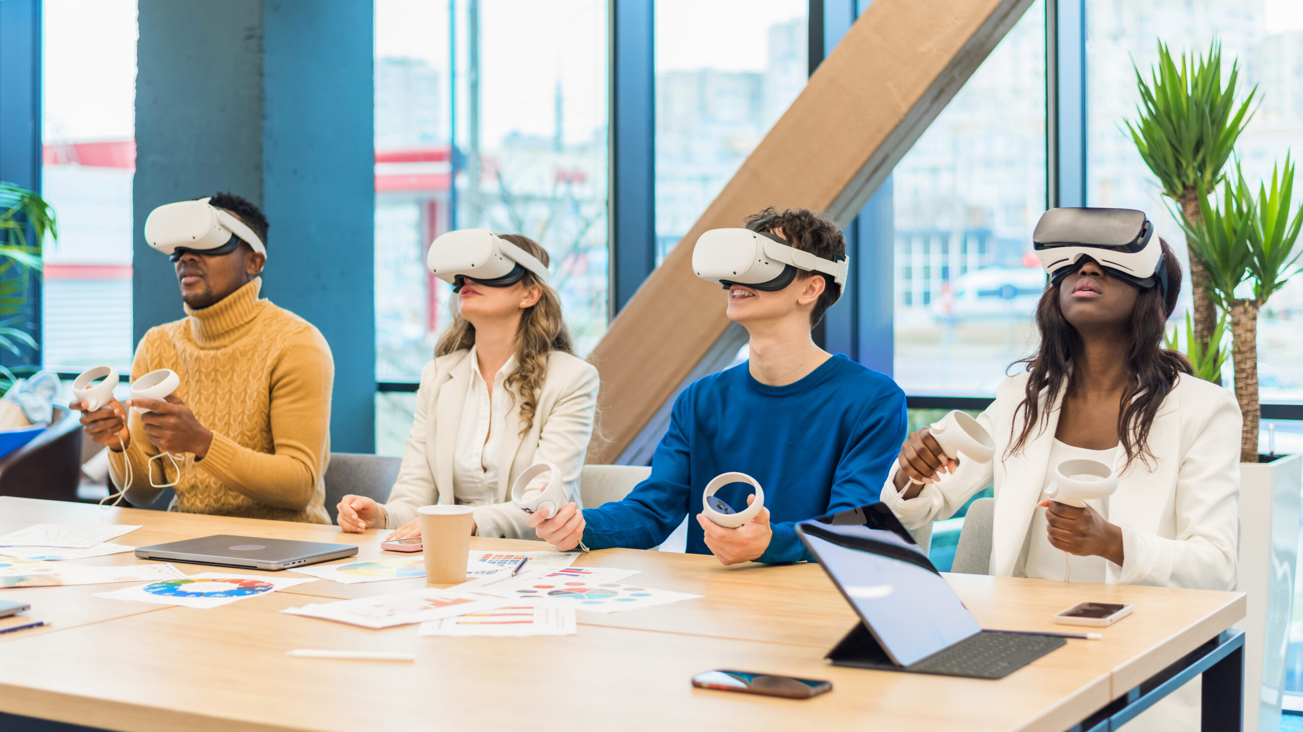 Business conference in VR in an office. Multiracial group of people using VR glasses and controllers, papers and gadgets on the table